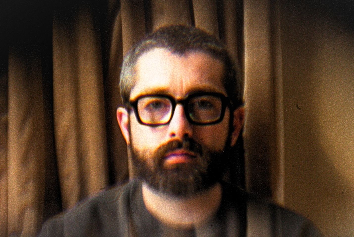 Man with glasses posing infront of curtain